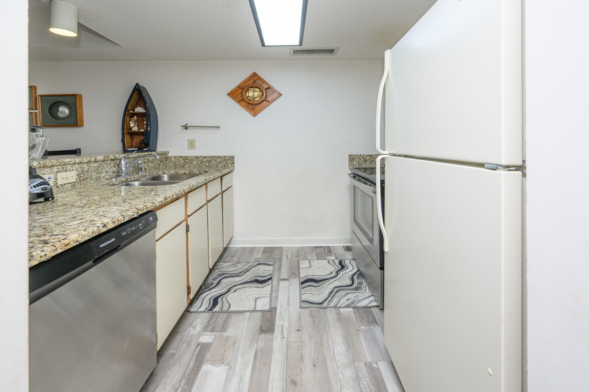 A compact kitchen with a dishwasher, double sink, and a refrigerator.