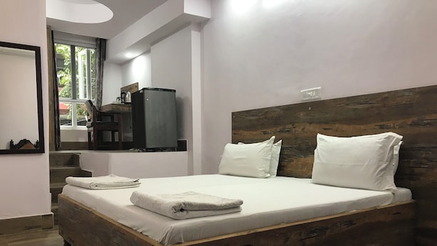A bedroom with a wooden bed, white bedding, and a small kitchenette area with a coffee maker. - Tatvamasi Homestay (New Delhi)