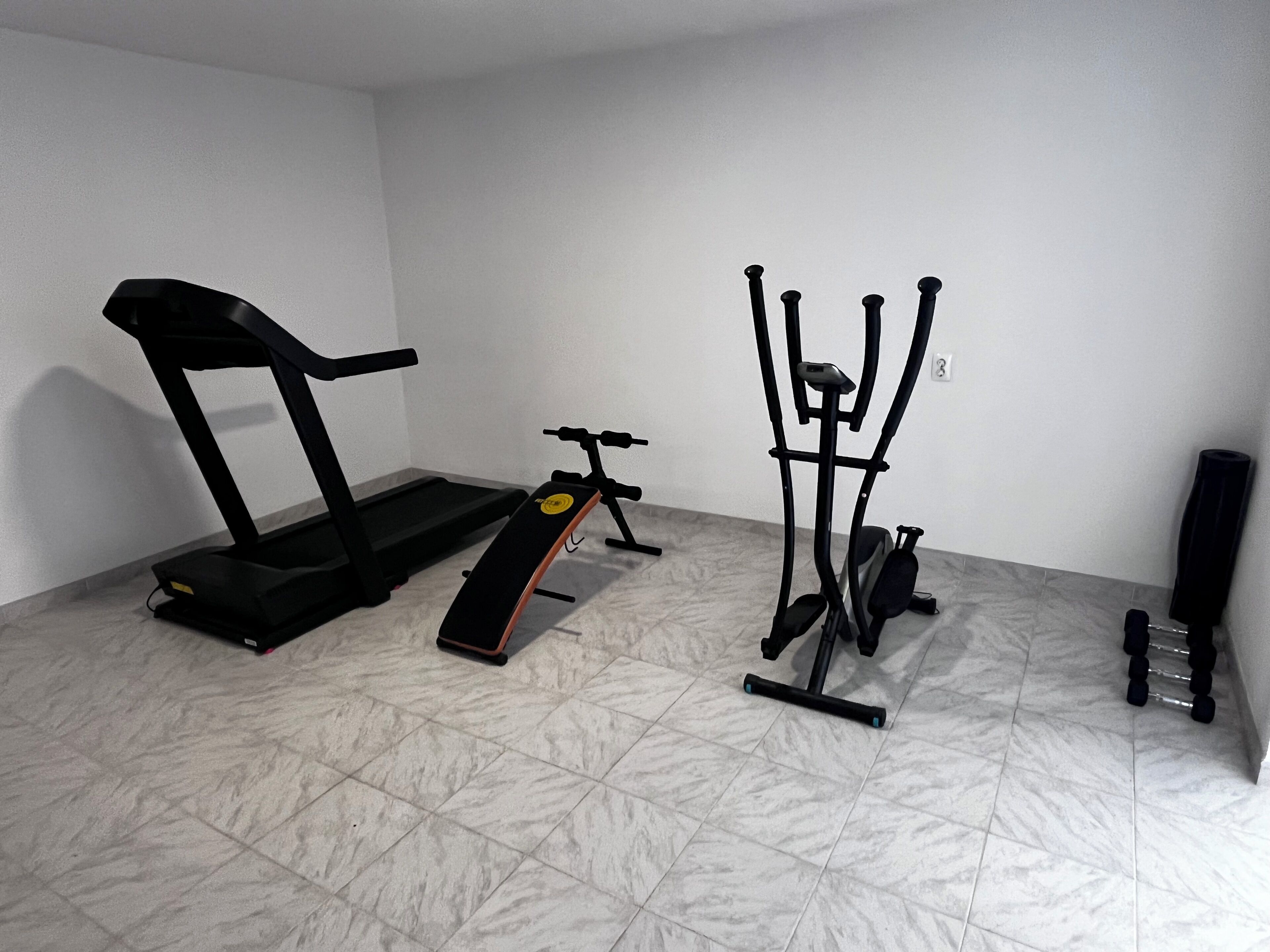 Een kamer met een loopband, elliptische trainer en een hometrainer.
