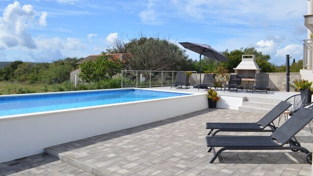A swimming pool with lounge chairs and a barbecue area. - Apartman Barbara (Sveti Filip i Jakov)