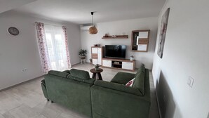 A living room with a green sofa, a television, and a small table with a plant. - Apartman Barbara (Sveti Filip i Jakov)