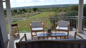 A balcony with two wooden chairs and a small table, overlooking a rural landscape with fields and a distant building. - Apartman Barbara (Sveti Filip i Jakov)