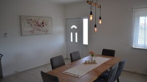 A dining area with a wooden table, six chairs, a floral centerpiece, and a hanging light fixture. - Apartman Barbara (Sveti Filip i Jakov)