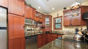 Una cucina con mobili in legno, piani in granito, elettrodomestici in acciaio inossidabile e una finestra con vista sugli alberi.