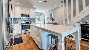 Una cocina moderna con armarios blancos, una isla central, electrodomésticos de acero inoxidable y piso de madera.