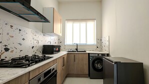 A compact kitchen with a gas stove, microwave, sink, and built-in washing machine. - Glassvine - 2D (Lagos)