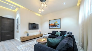 A modern living room with a dark sofa, a coffee table, a TV mounted on the wall, and a painting above the sofa. - Glassvine - 2D (Lagos)