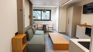 Une pièce compacte et moderne, dotée d’un canapé, d’une table en bois et d’un coin repas avec des chaises.