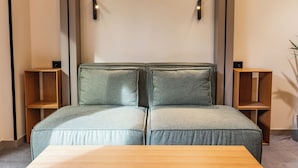 Une chambre moderne avec un canapé-lit, des tables d’appoint en bois et une petite table placée au premier plan.