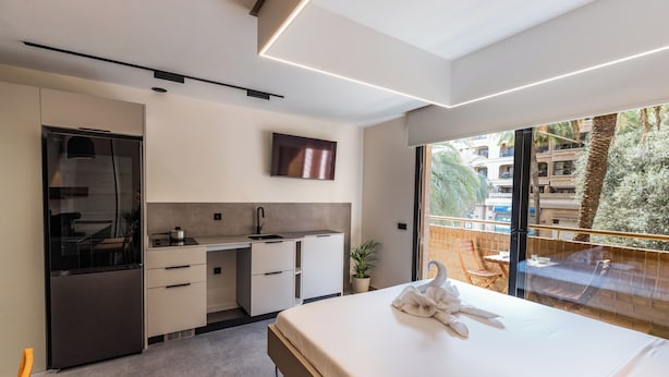 Une chambre d’hôtel moderne dotée d’une kitchenette, d’un grand lit, d’une télévision et d’un balcon offrant une vue sur la ville.