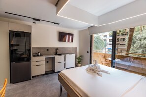 A modern hotel room with a kitchenette, a large bed, a TV, and a balcony with a view of the city. - Motus Disruptive Apartments (València)