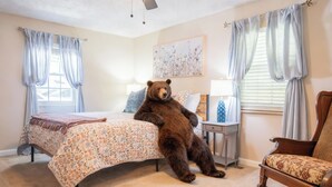 Ein Schlafzimmer mit einem großen Bett, einem Sessel, einem Nachttisch, einer Lampe, einem Deckenventilator und einem Fenster mit Vorhängen.