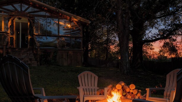 Eine rustikale Holzhütte mit Feuerstelle im Vordergrund, umgeben von Adirondack-Stühlen.