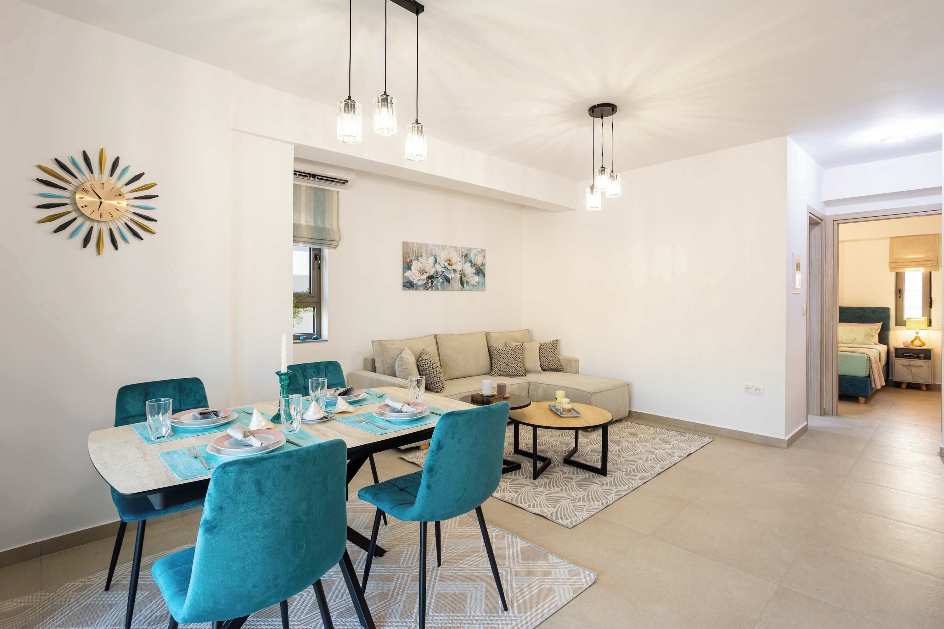 A dining area with a table set for four, teal chairs, and a modern chandelier.