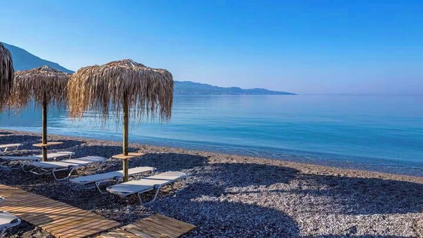 Una spiaggia con ciottoli, lettini e ombrelloni di paglia.