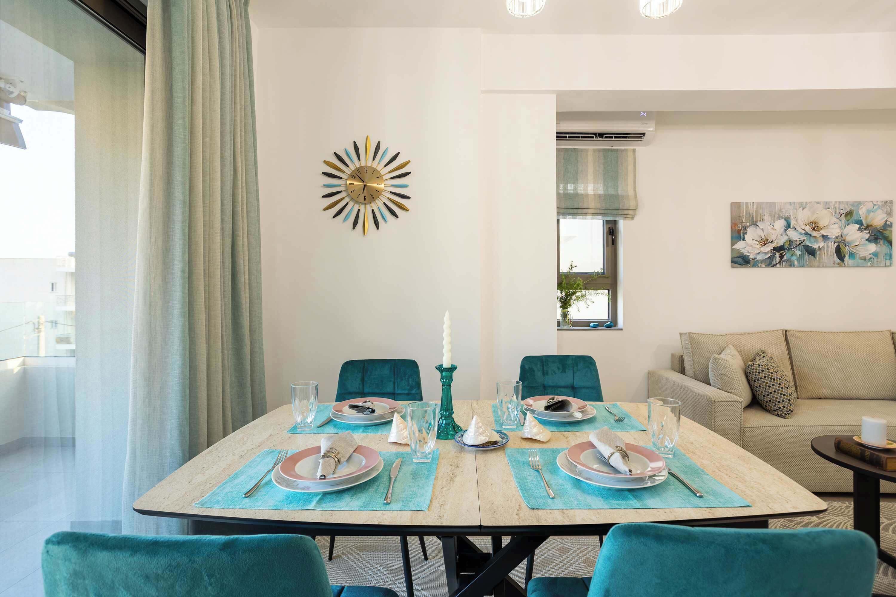 Comedor con una mesa redonda para cuatro, sillas color turquesa y un reloj de pared moderno.