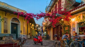 Una strada acciottolata fiancheggiata da edifici, uno scooter rosso e biciclette parcheggiate sul lato.