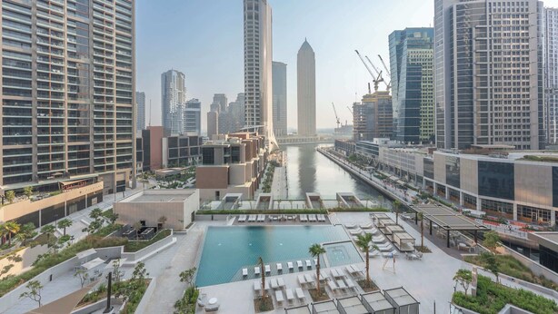 Zona urbana moderna con edificios altos, una vía fluvial central y un área de piscina en la azotea con sillones de descanso.