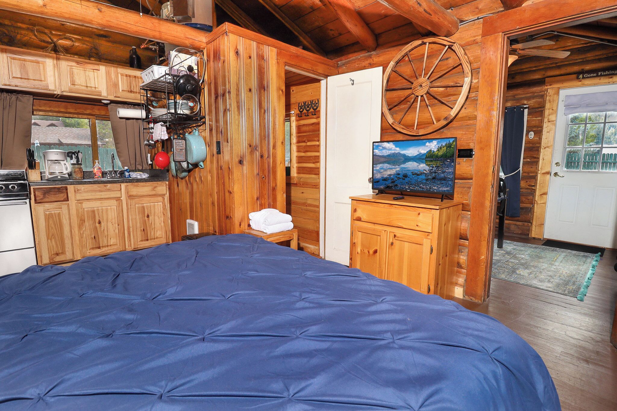 Ein Holzblockhaus-Innenraum mit einem Bett, einer Küchenzeile und einem Fernseher auf einer Holzkommode.