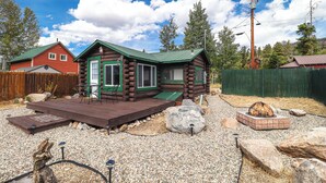 A log cabin with a green roof, a deck, and a fire pit.