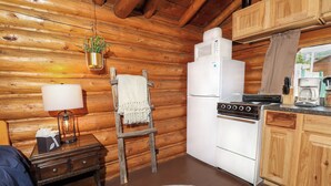 A cozy cabin-style kitchen with wooden walls, a white refrigerator, a stove, and a hanging plant.