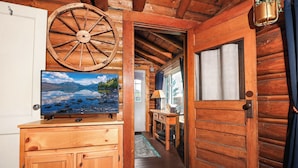 A wooden cabin interior with a television on a wooden cabinet, a wooden wheel, and a door leading to another room.