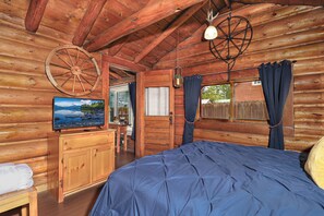 A log cabin room with a bed, wooden dresser, TV, and a large wheel hanging from the ceiling.