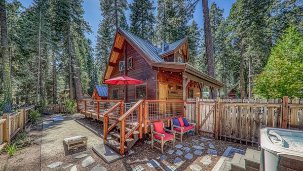 A cabin with a deck, outdoor seating, and a stone patio. - Classic Cabin in the Pines by Tahoe Getaways - Walk to Lake, Pet-Friendly 3 BR w/ Yard & Hot Tub! (Homewood)