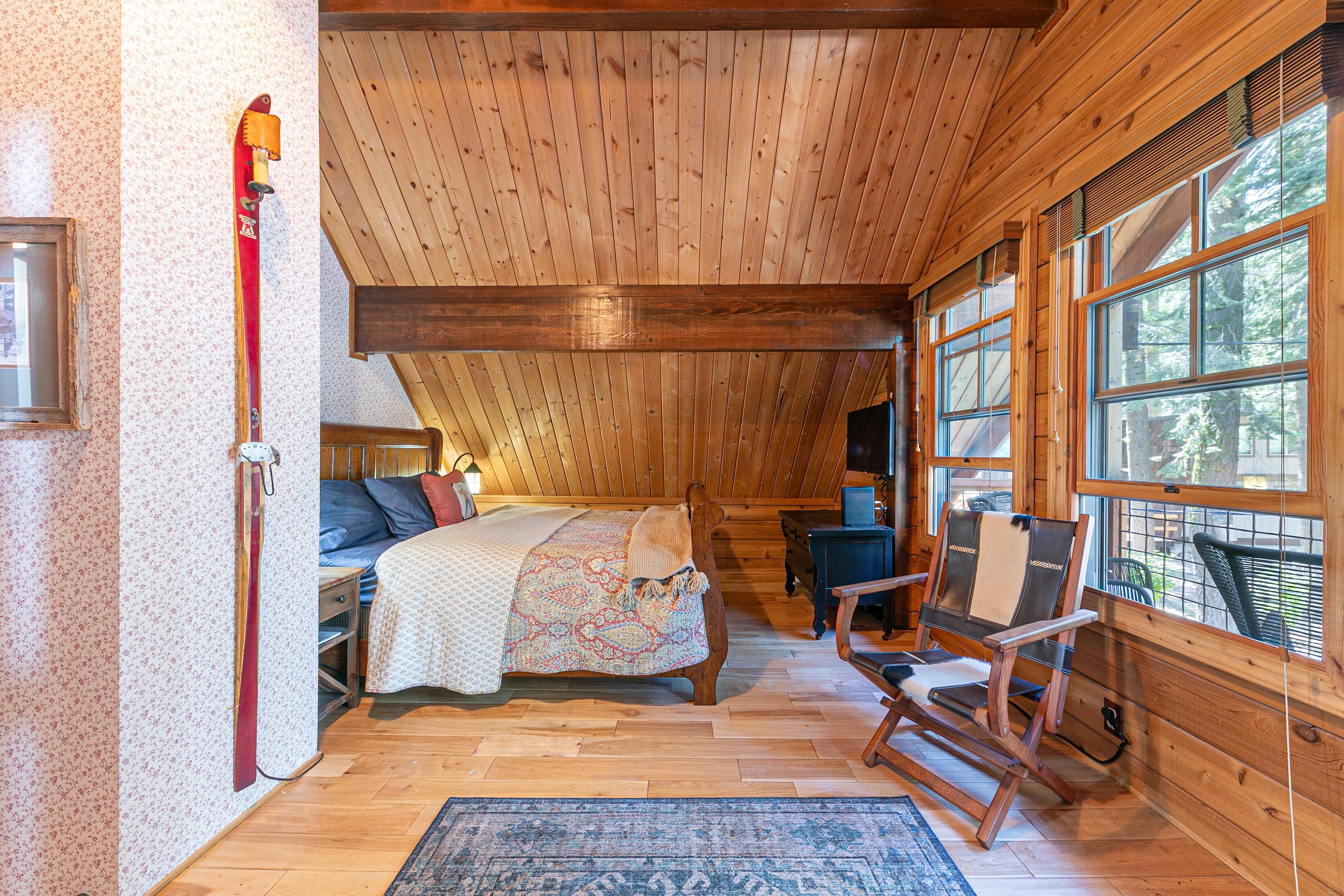A wooden cabin bedroom with a bed, a rocking chair, and a large window.