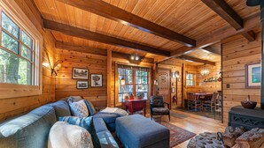 A cozy log cabin interior with a large wooden-framed living room, a dining area, and a fireplace. - Classic Cabin in the Pines by Tahoe Getaways - Walk to Lake, Pet-Friendly 3 BR w/ Yard & Hot Tub! (Homewood)