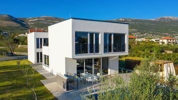 Ein modernes, zweistöckiges Haus mit Terrasse, großen Fenstern und Blick auf die umliegende Landschaft.
