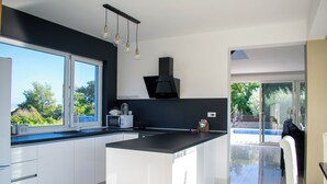 Cocina moderna con una isla grande, armarios blancos y una campana extractora negra. Se ve follaje verde a través de una ventana.