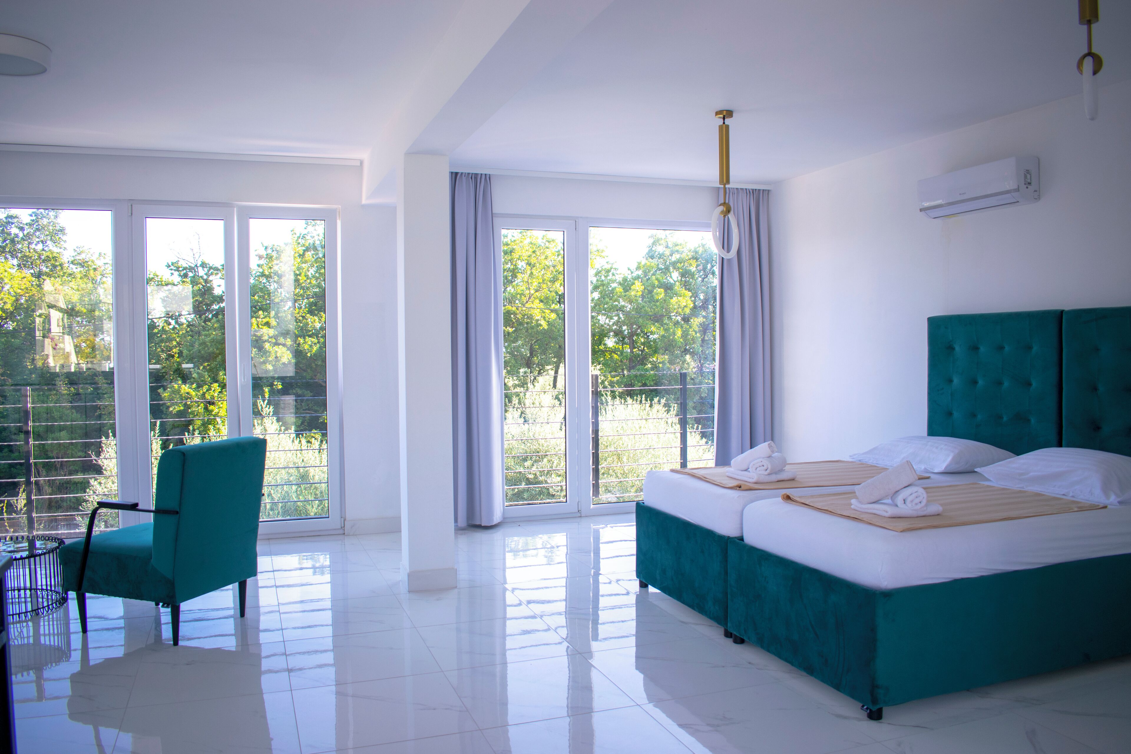 Ein Hotelzimmer mit einem großen Bett, einem Sessel und Blick auf Grün durch die Fenster.