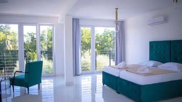Ein Hotelzimmer mit einem großen Bett, einem Sessel und Blick auf Grün durch die Fenster.