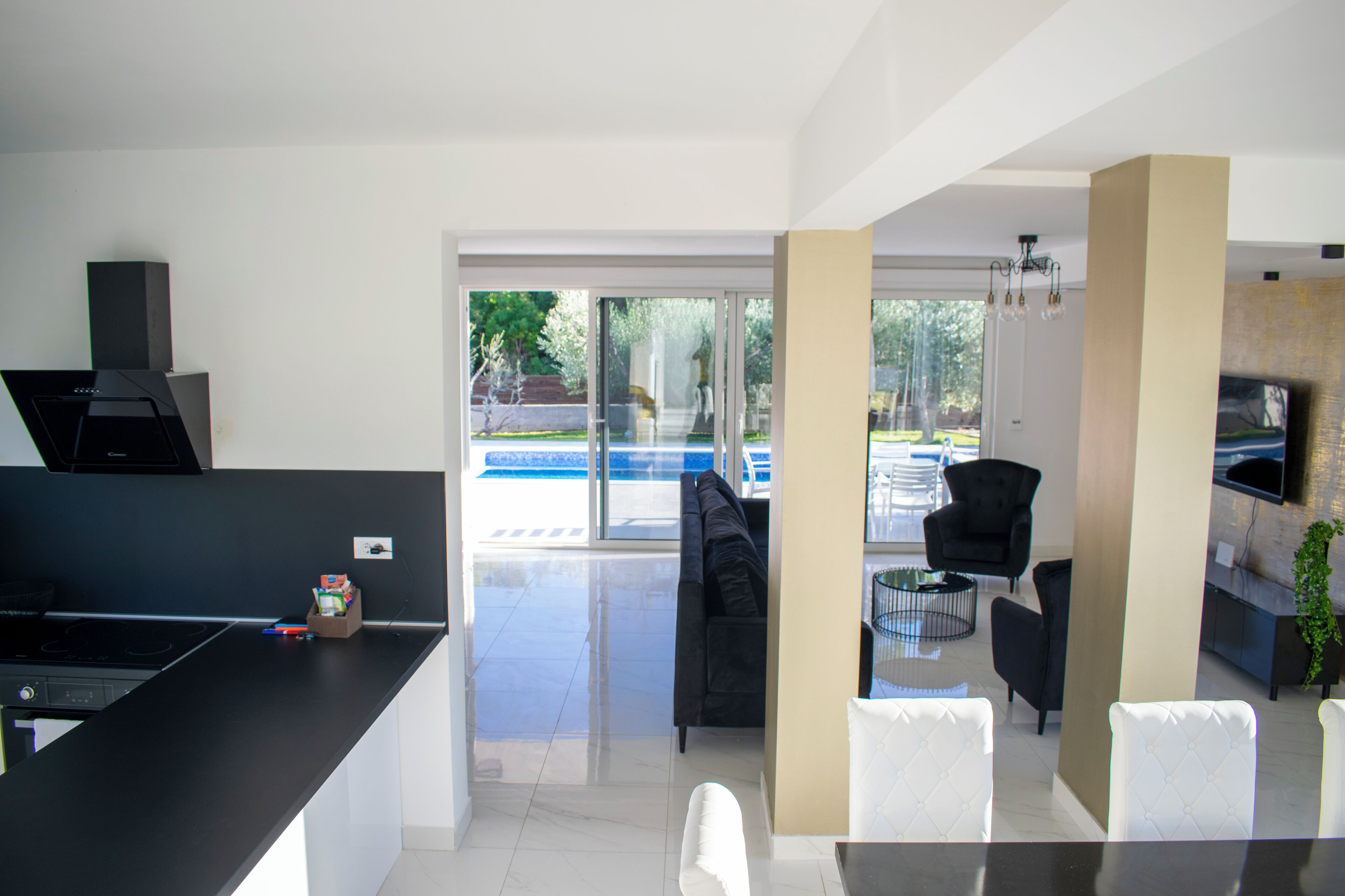 A modern kitchen with a black countertop, a built-in stove, and a small refrigerator. There is a glass door leading to a patio with a pool and outdoor furniture.