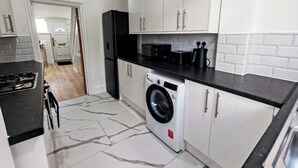 A modern kitchen with white cabinets, a black refrigerator, a washing machine, and a black countertop. - 6 en-suite Rooms all king beds  (Ilford)