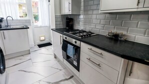 A modern kitchen with white cabinets, a black countertop, a gas stove, and a tiled backsplash. - 6 en-suite Rooms all king beds  (Ilford)