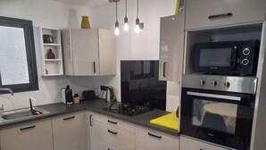 A modern kitchen with white cabinets, a gas stove, a microwave, and a built-in oven. - Comfortable house in a quiet area close to the sea and amenities in a seaside resort. (L'Étang-Salé les bains)
