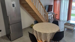 A compact kitchen with a stainless steel refrigerator, a wooden staircase, a dining table with chairs, and a small TV. - Comfortable house in a quiet area close to the sea and amenities in a seaside resort. (L'Étang-Salé les bains)