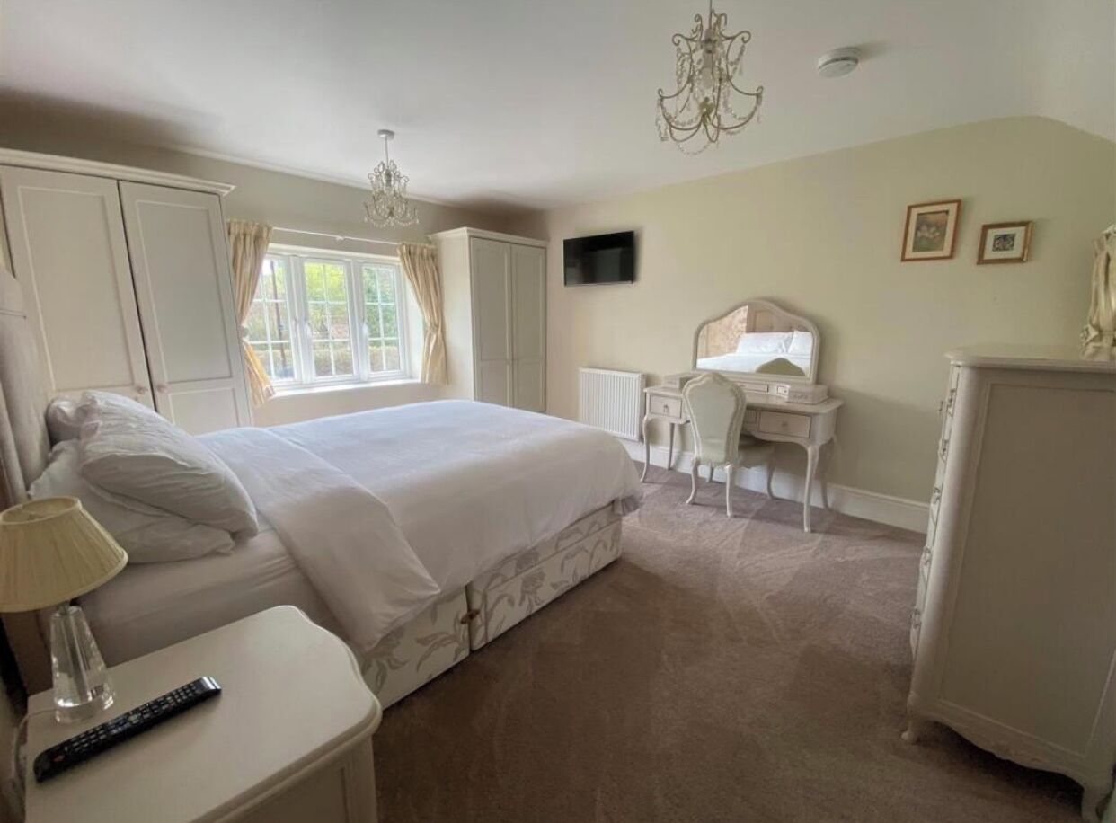 A bedroom with a bed, bedside table, lamp, and a desk with a chair.