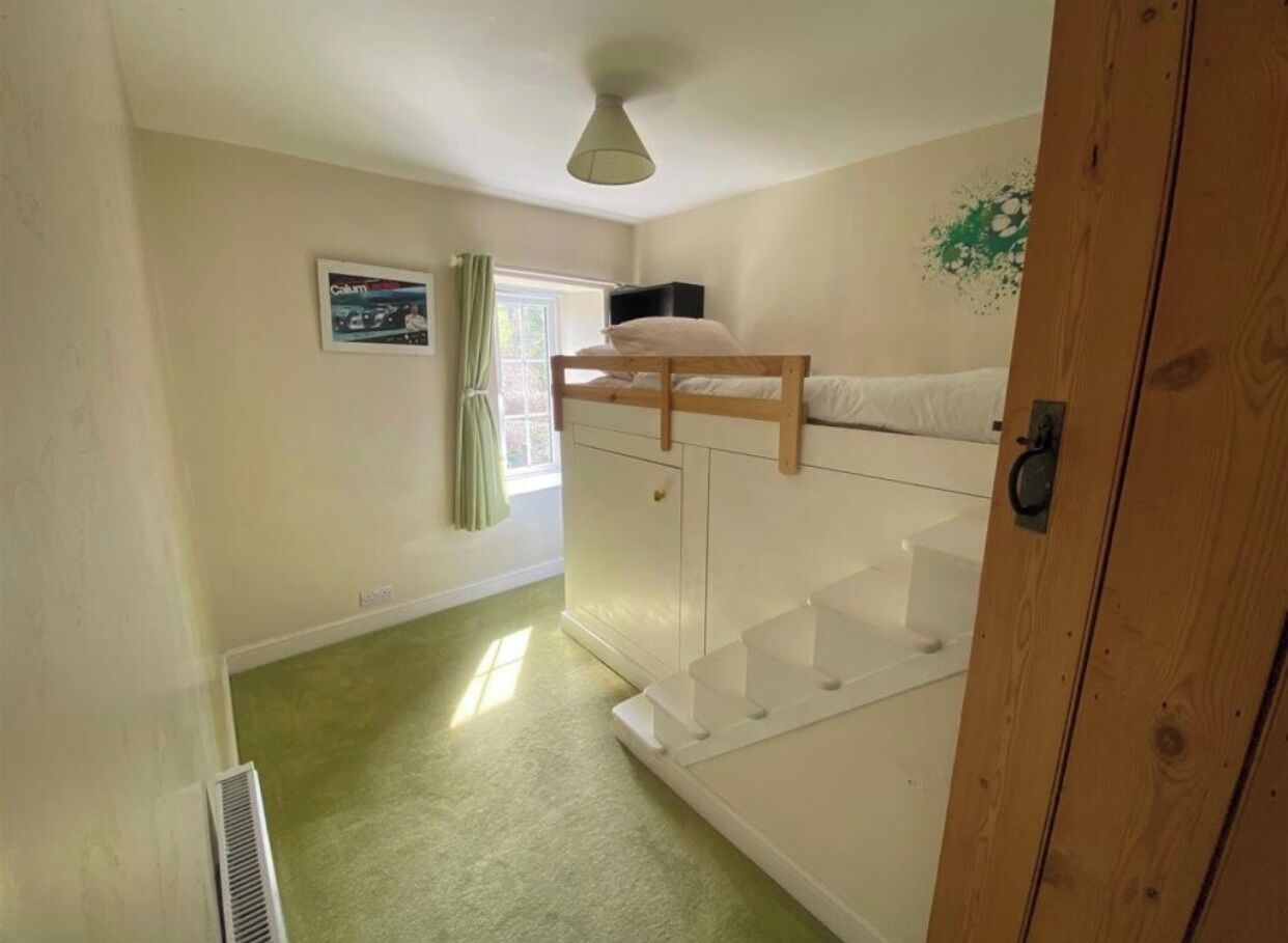 Ein Zimmer mit Etagenbett, kleinem Schreibtisch, Heizkörper und einem Fenster mit Vorhängen.