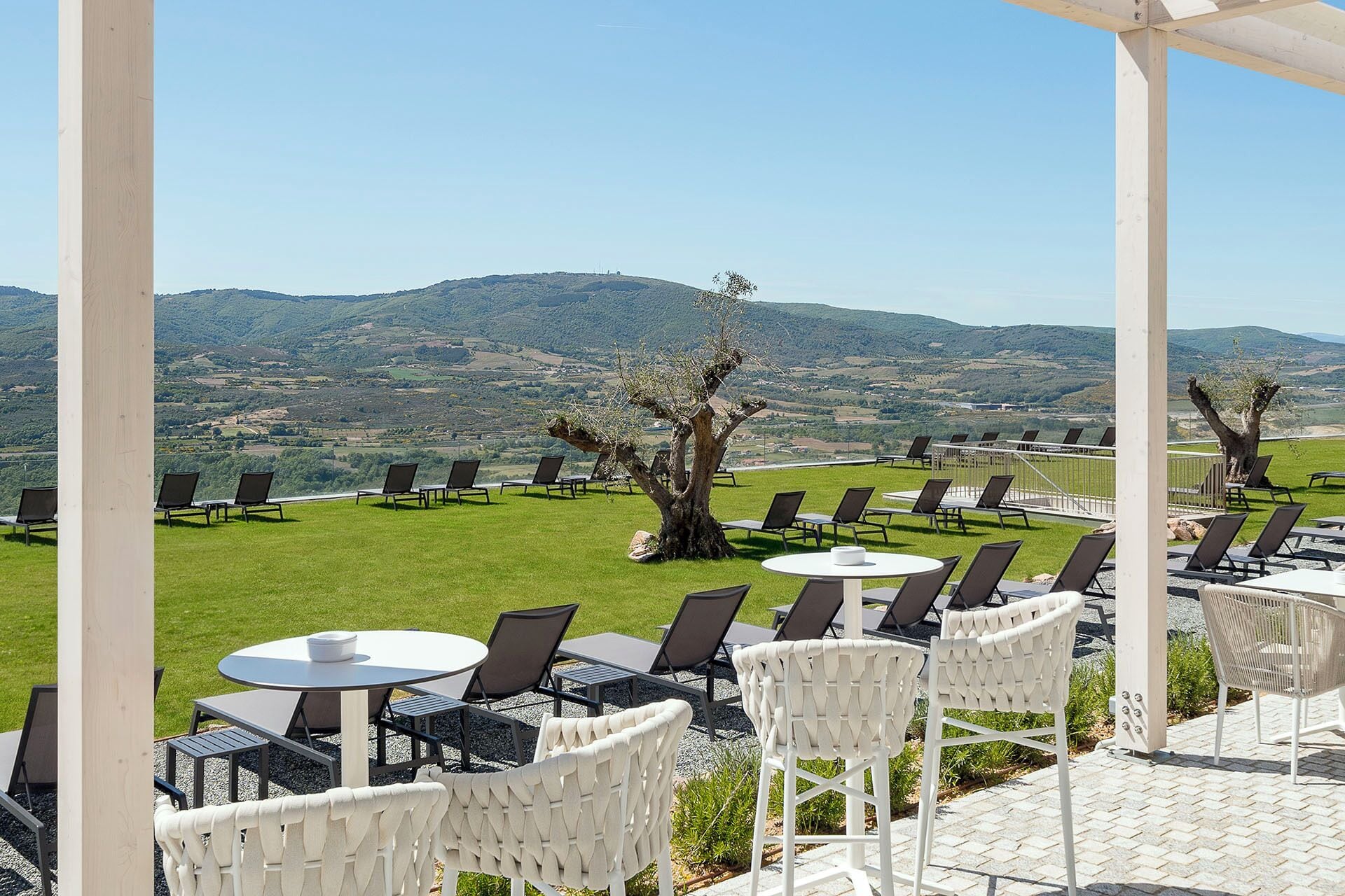 A terrace with outdoor seating, a view of rolling hills, and a tree in the center.