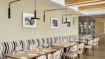 A modern restaurant with striped seating, long tables, and pendant lighting.