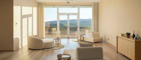A spacious room with a large sliding glass door leading to a balcony with a mountain view. There are two sofas, a small round table, and a cabinet.