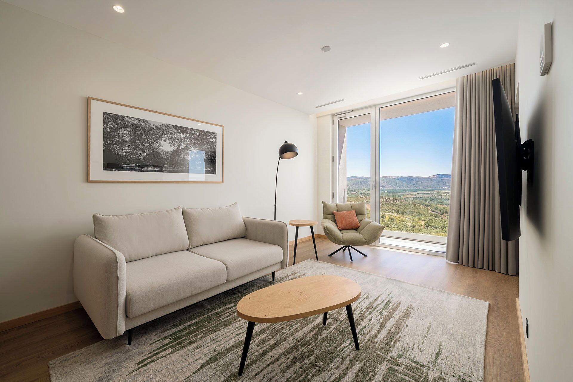 Una sala de estar moderna con sofá, una mesa de centro, una lámpara de pie y vistas al exterior.