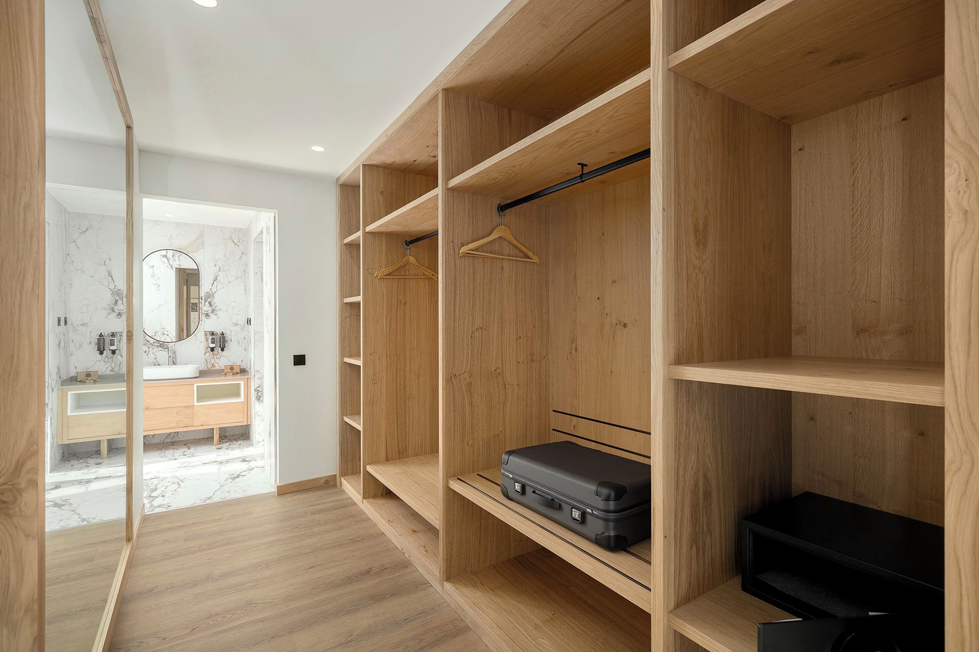 A walk-in closet with wooden shelving, a hanging rod, and a suitcase on the lower shelf.