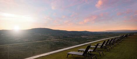 Una fila de sillones de exterior en una pendiente cubierta de césped, con vista a un valle y colinas distantes.