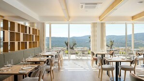 Un restaurante con vista a las montañas, muebles de madera y grandes ventanales.
