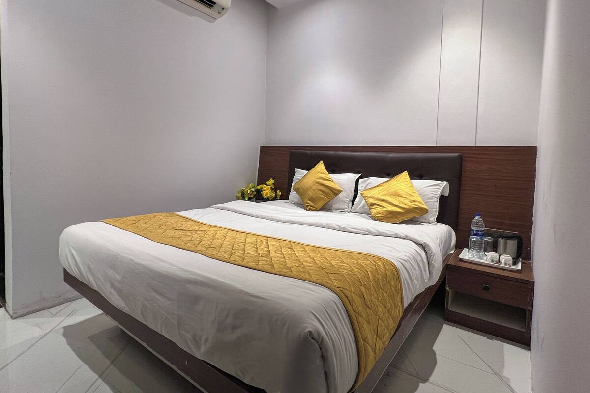Ein Hotelzimmer mit einem großen Bett, einem Holzkopfende, einem Nachttisch mit einer Wasserflasche und einer Klimaanlage an der Wand.