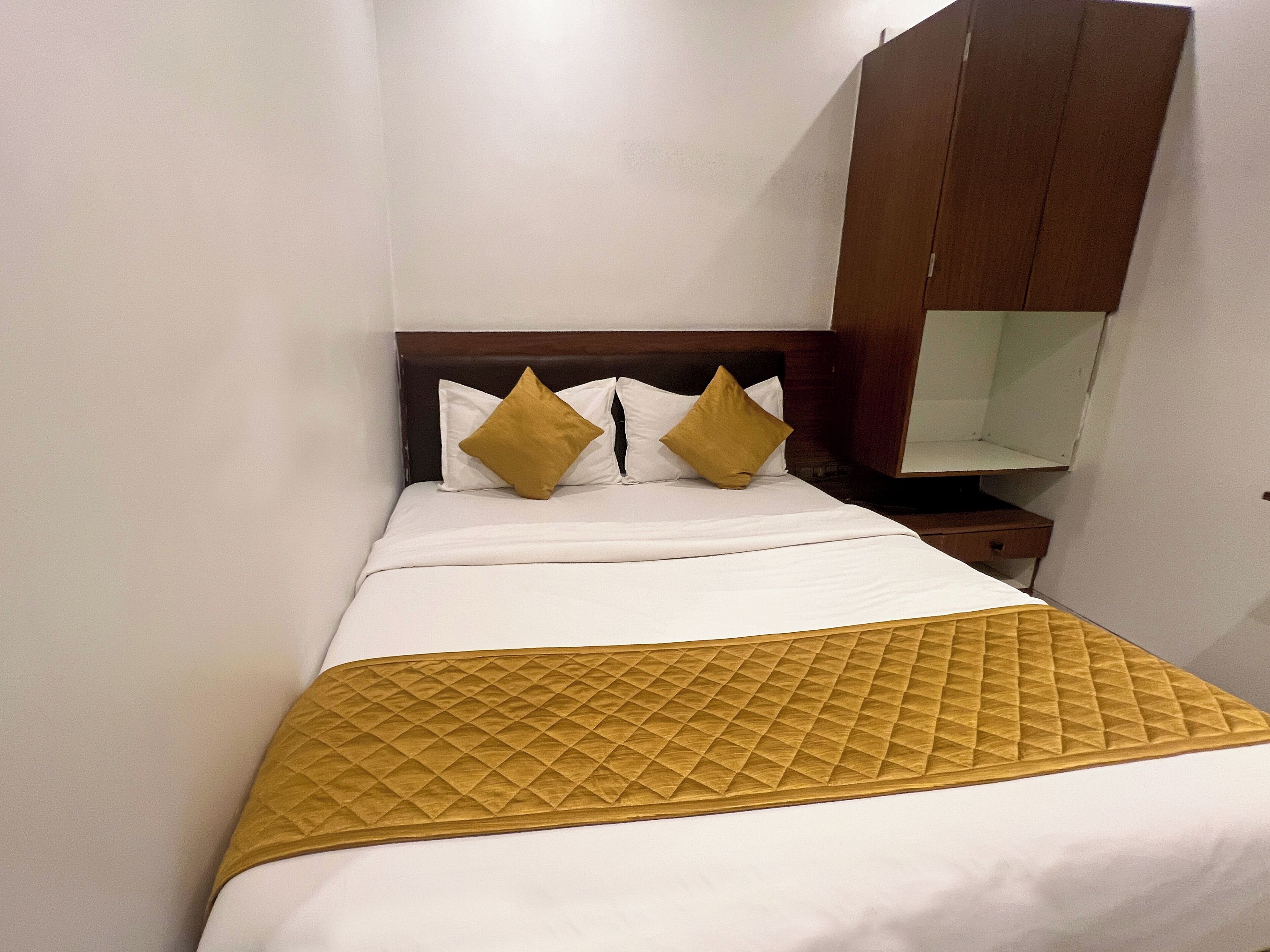 A neatly made bed with white linens and two gold pillows, a wooden headboard, and a small bedside table with a mirror.